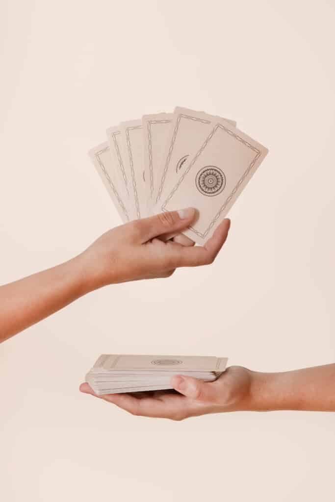 Lecture de cartes : mains tenant un jeu de tarot Deux mains : une tenant un éventail de cartes à tarot vierges aux dos ornés, l'autre tenant la pile restante.